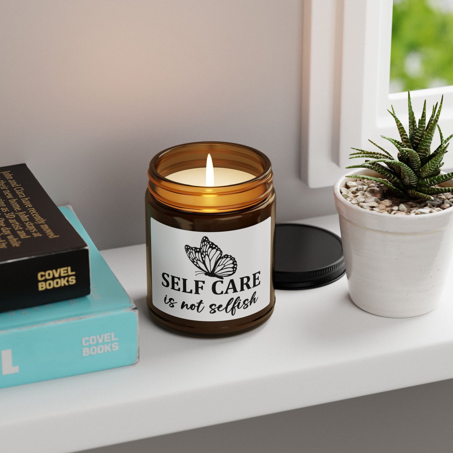 Candle in an amber jar with a label reading 'Self care is not selfish' on a shelf with books and a plant.