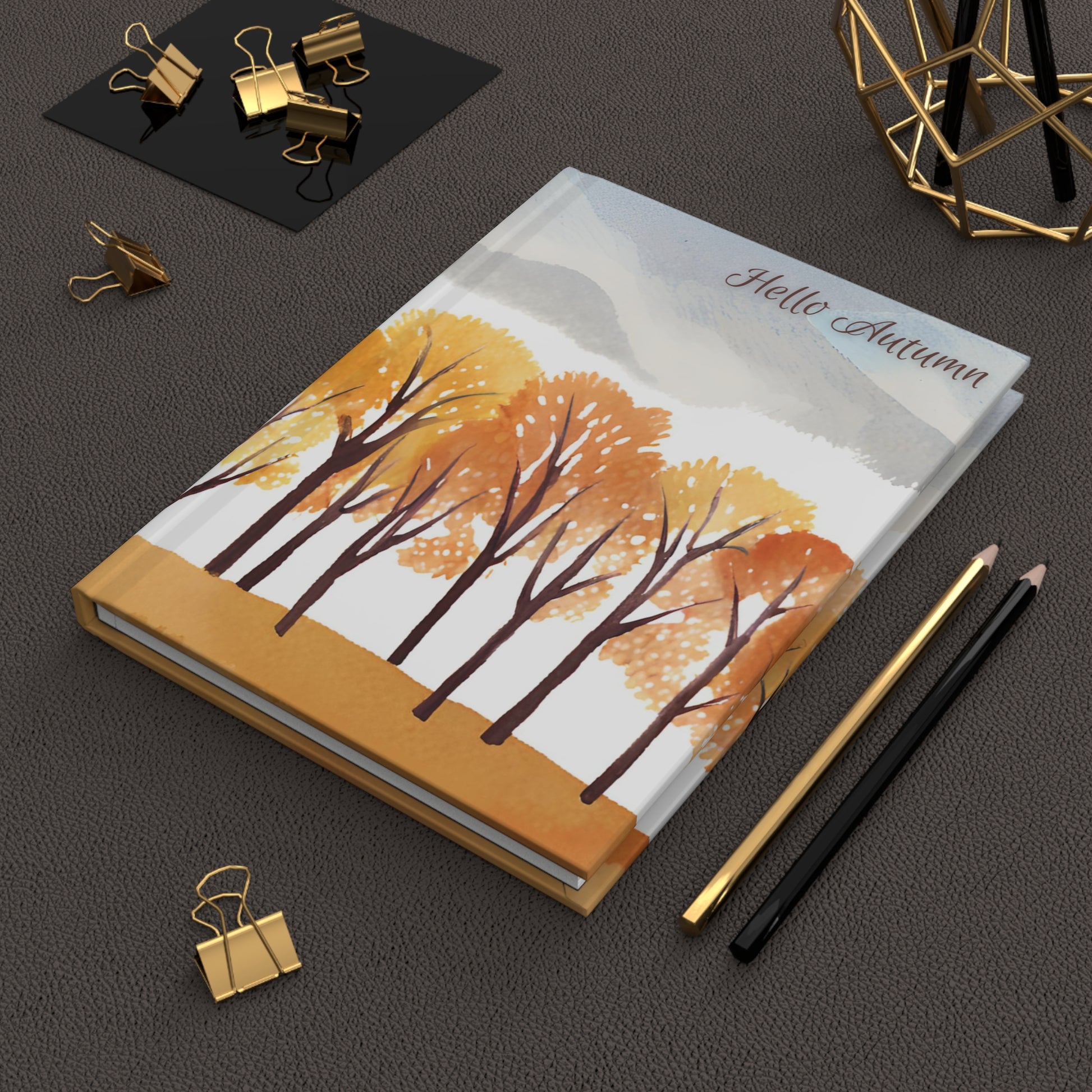 Notebook with autumn design on a dark surface with stationery items.
