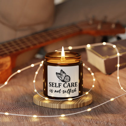 Candle with 'Self Care is not Selfish' label on a wooden coaster with fairy lights, guitar in the background