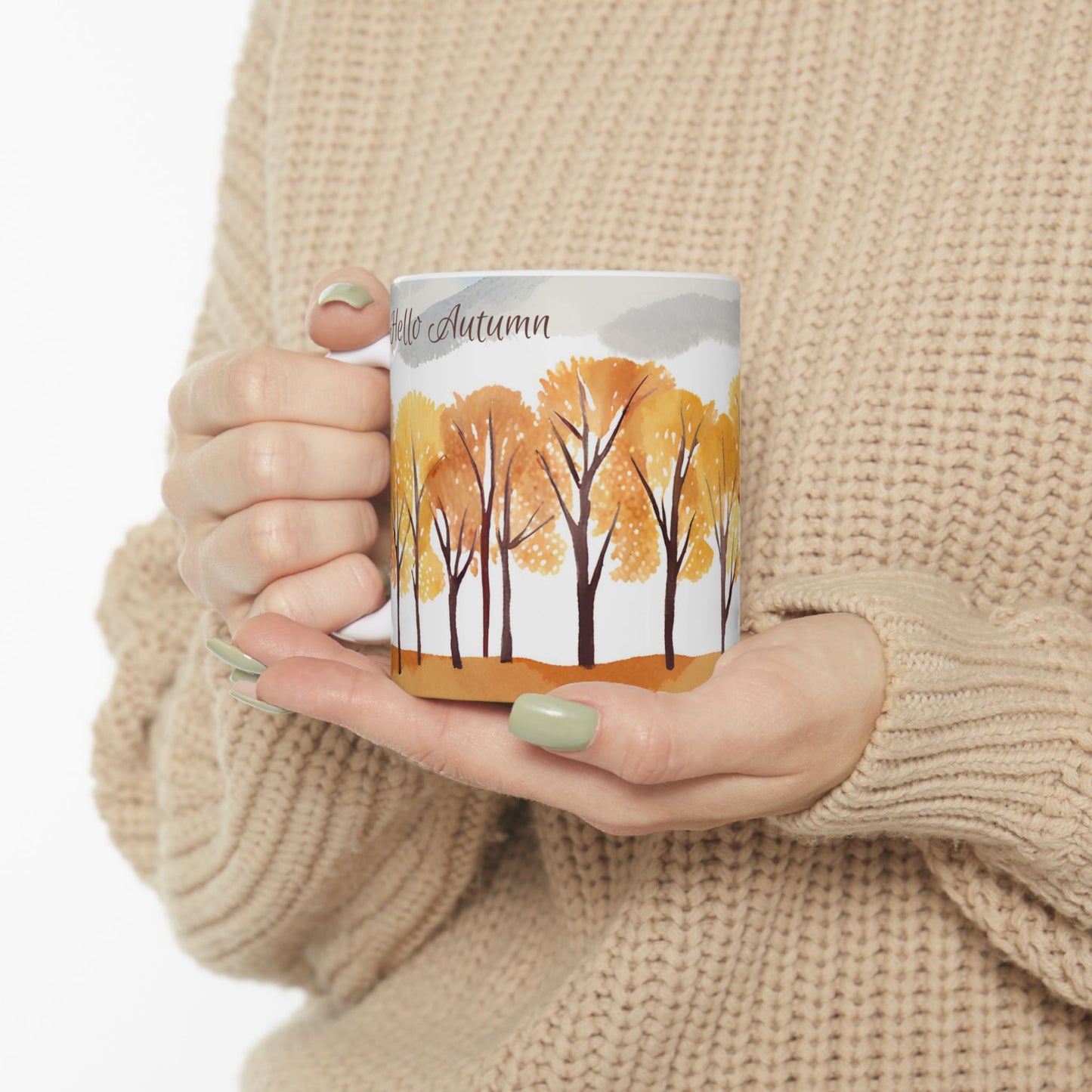 Person holding a mug with autumn tree design and 'Hello Autumn' text.