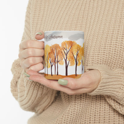 Person holding a mug with autumn tree design and 'Hello Autumn' text.