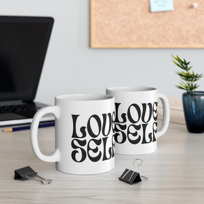 Two white mugs with 'LOVE SELF' text on a desk with office items.
