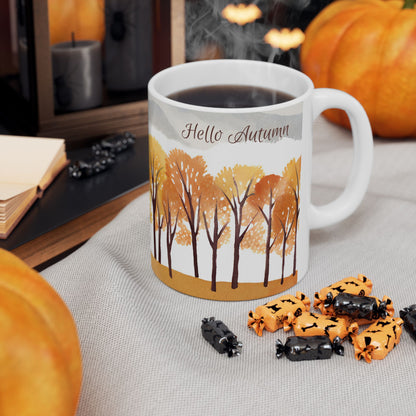 White mug with autumn-themed design featuring trees and 'Hello Autumn' text, surrounded by Halloween treats and pumpkins.