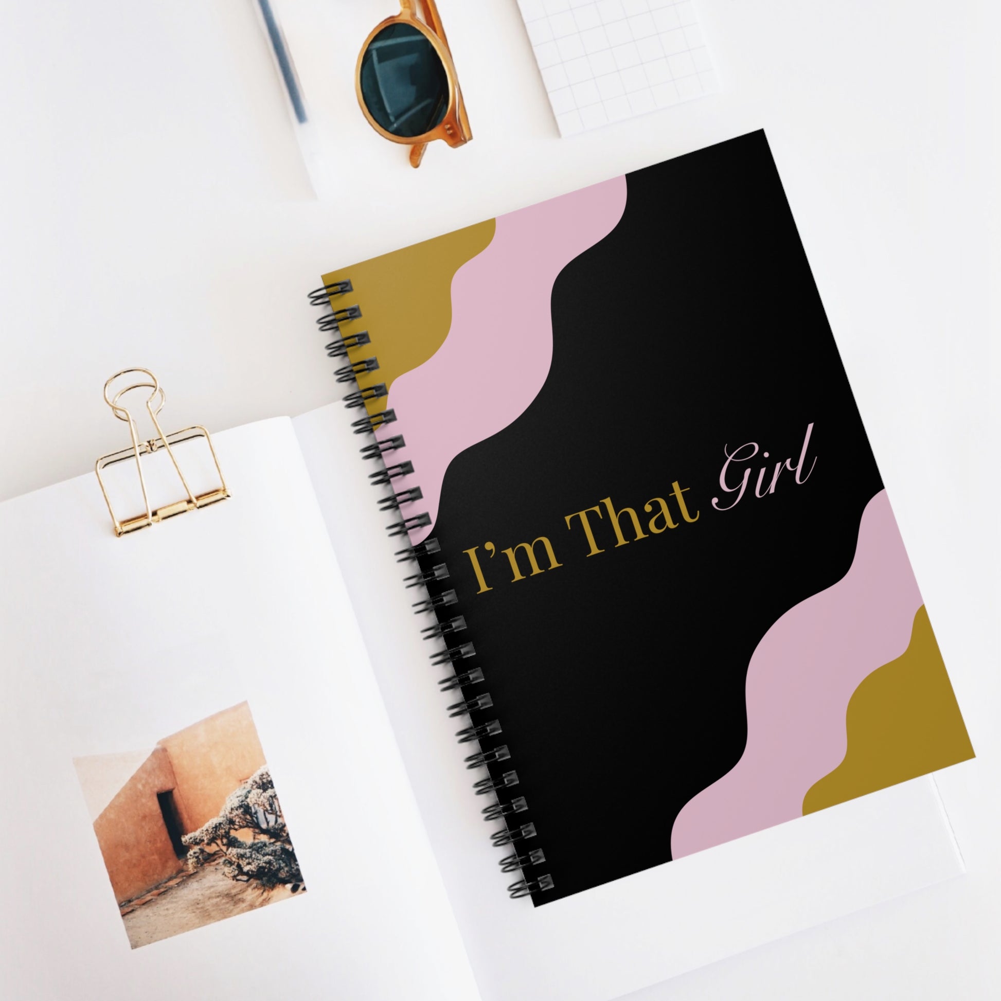 Notebook with 'I'm That Girl' design on a white surface with sunglasses and a photo clip.