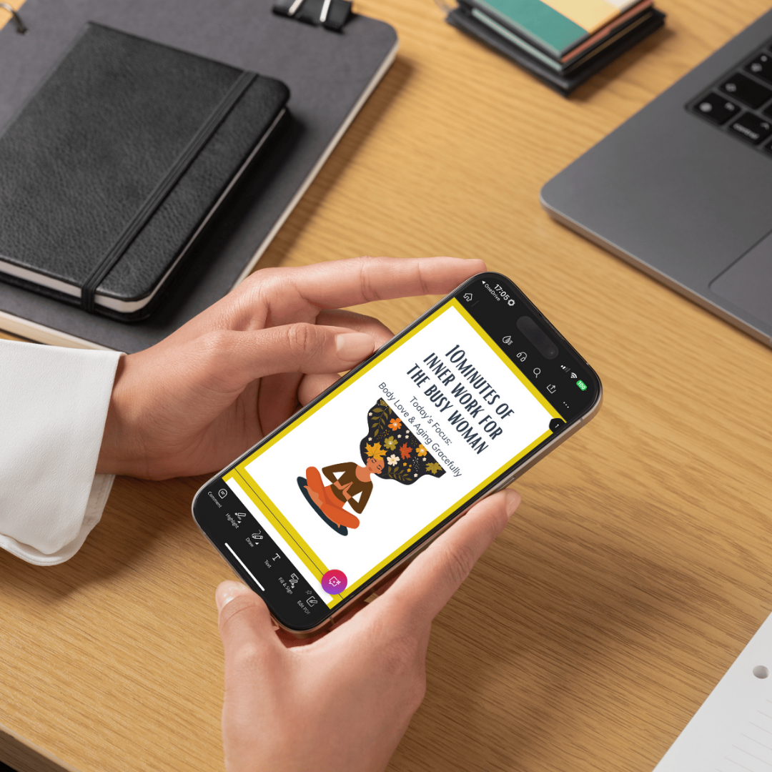 Person holding a smartphone with an app open on a desk with notebooks and a laptop.
