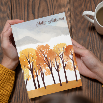 Person holding a card with autumn design and 'Hello Autumn' text, next to a cup of coffee on a wooden table.