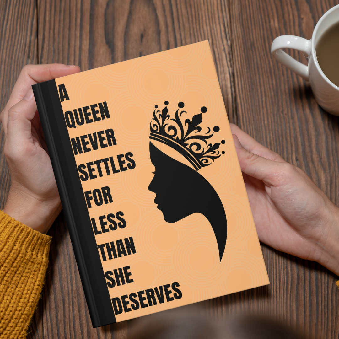 Notebook with a queen design and text on a wooden table with a cup of coffee.