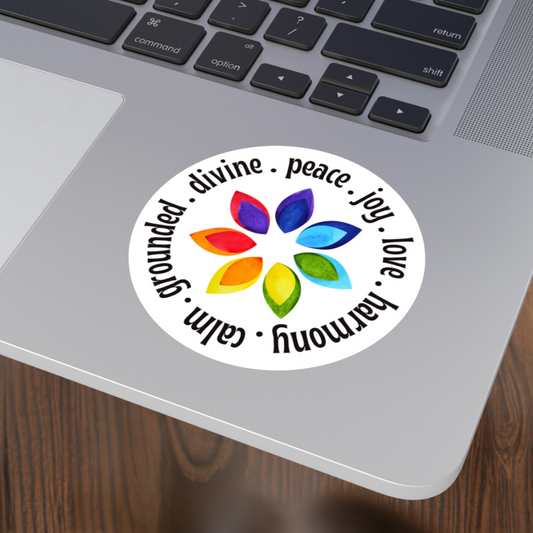 Laptop with a colorful sticker featuring a rainbow flower design and motivational words on a wooden surface.