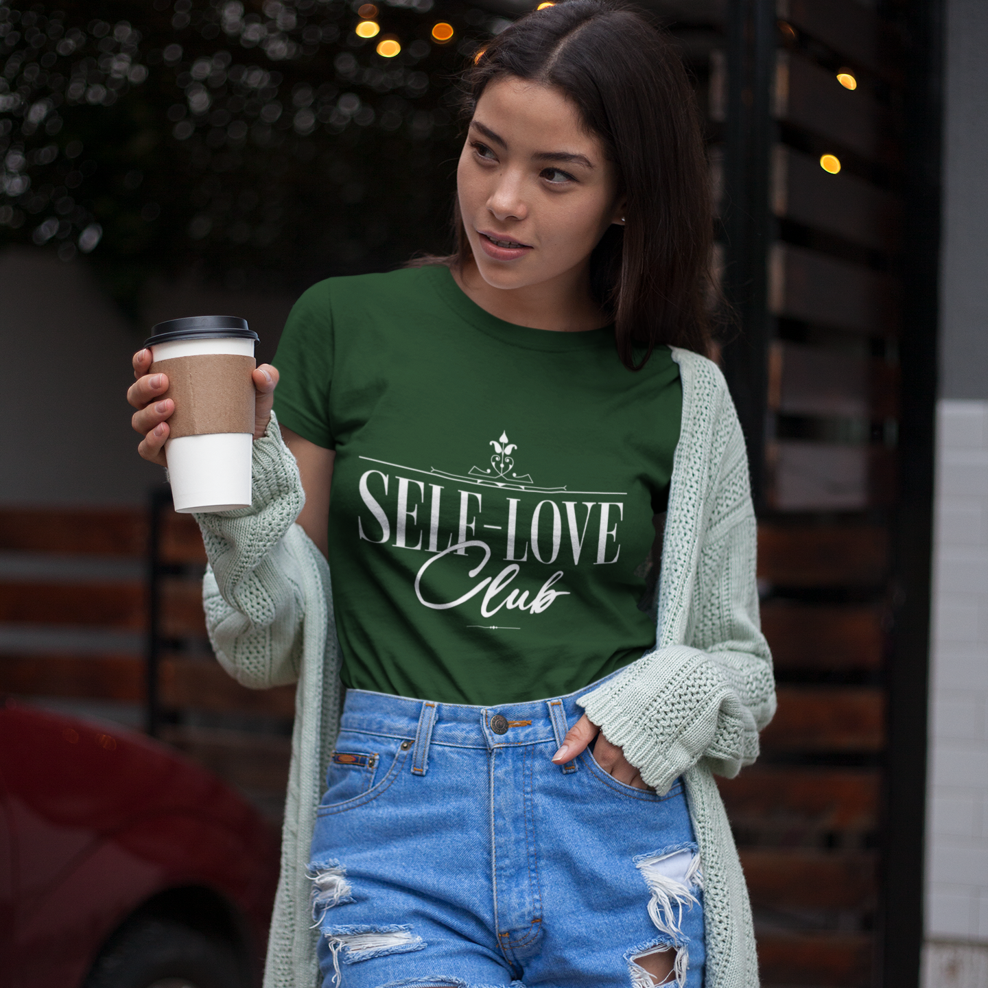 Woman wearing a green 'Self-Love Club' t-shirt holding a coffee cup.