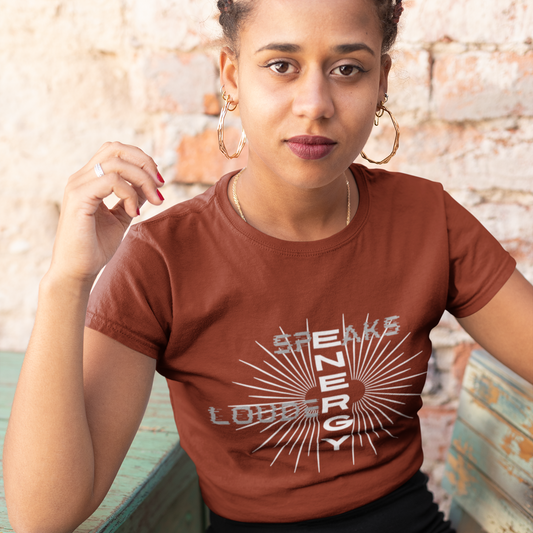 Woman wearing a brown t-shirt with 'Speak Energy Loud' design against a textured wall.