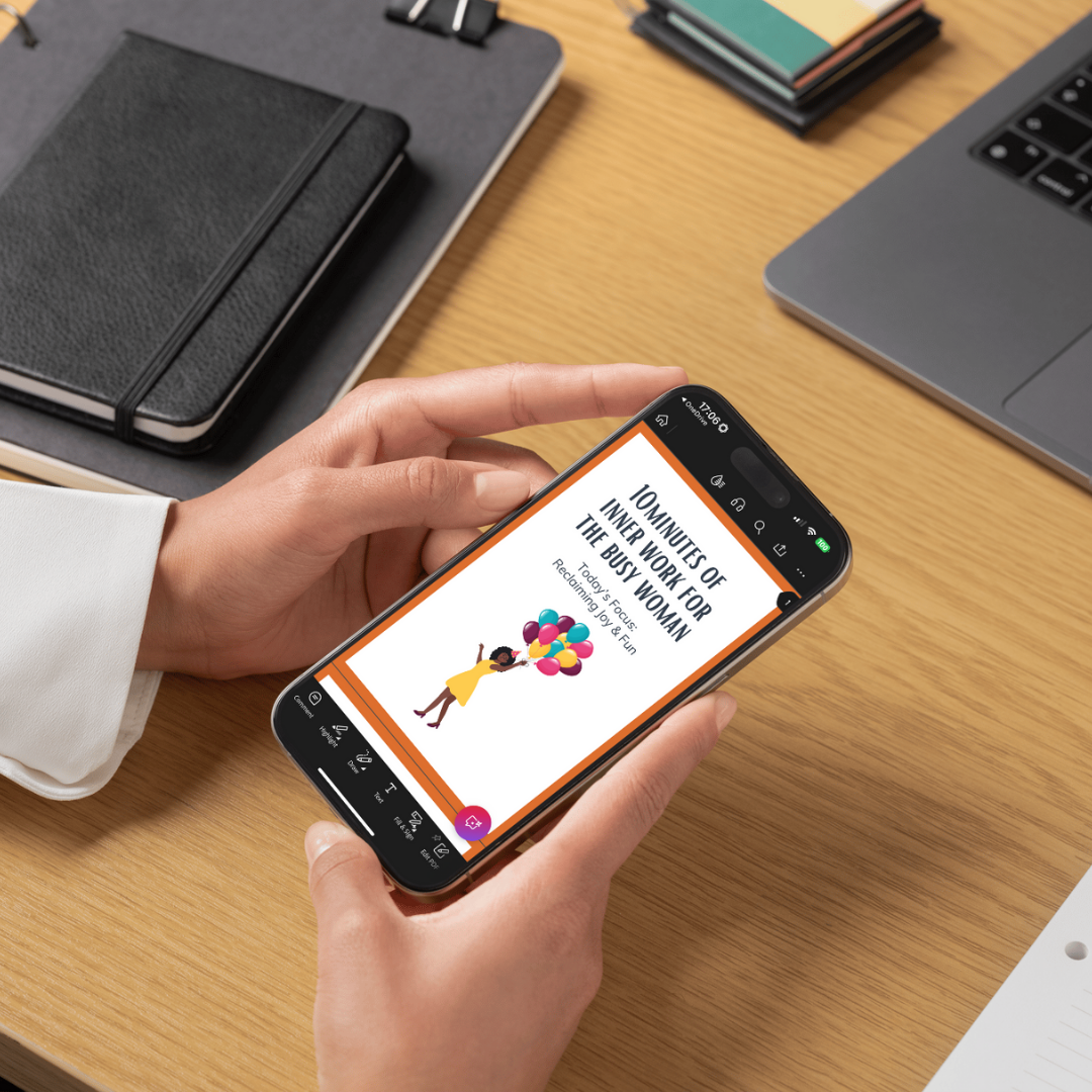 Person holding a smartphone with a colorful app interface on a desk with notebooks and a laptop.