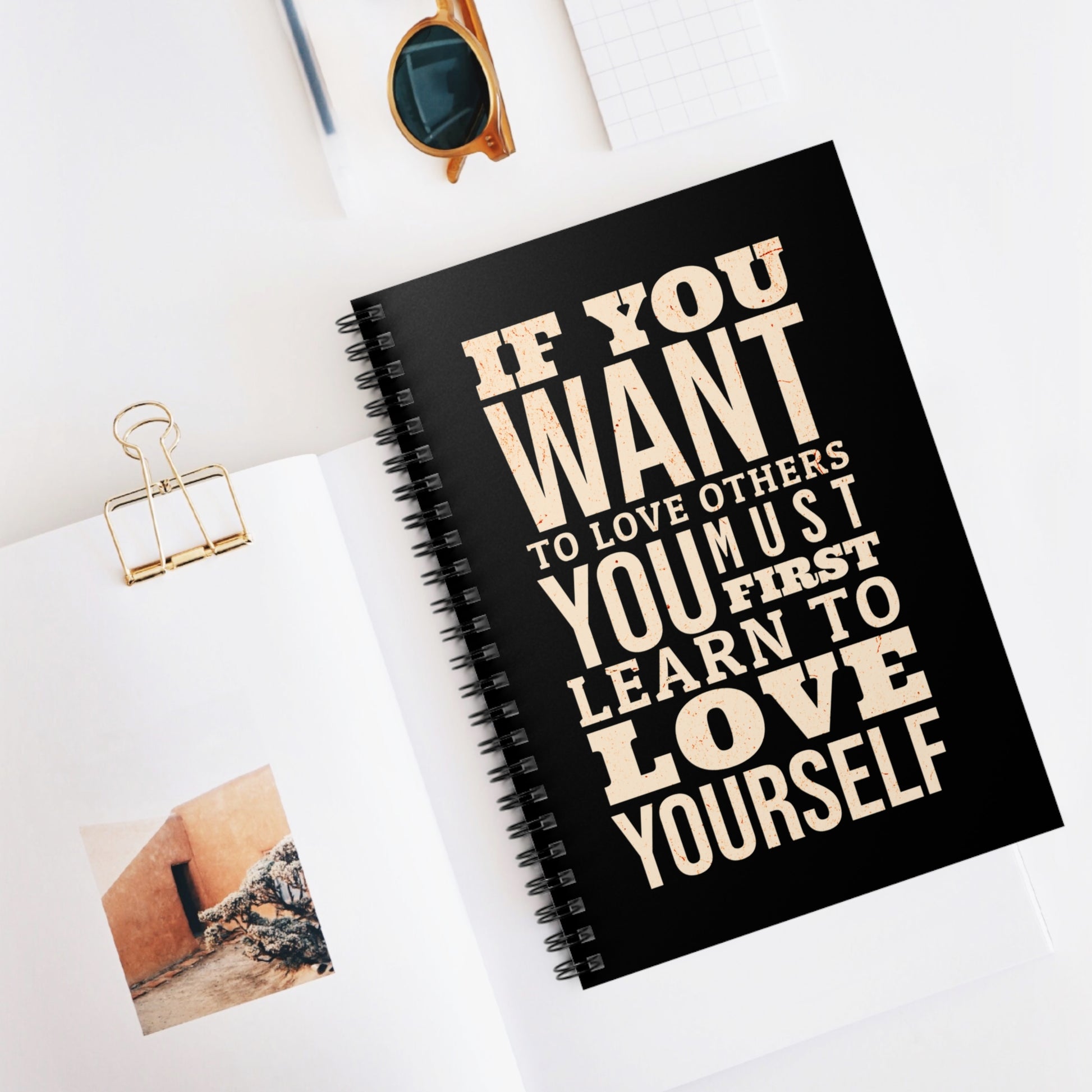 Black notebook with motivational quote on a white surface with sunglasses and photo clips.