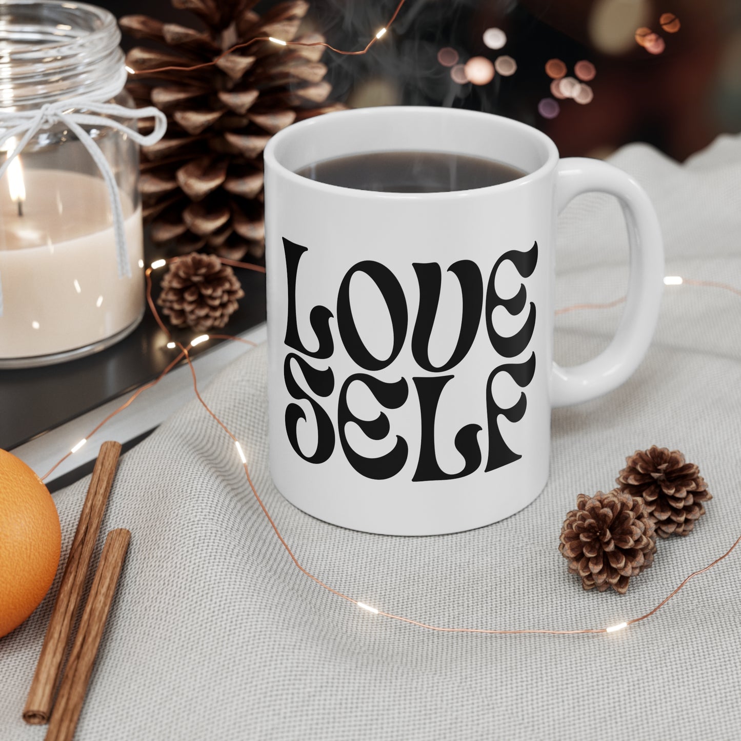 White mug with 'LOVE SELF' text on a table with decorative items
